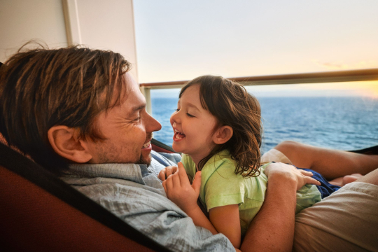 Vater mit Kind auf dem Arm in einer Hängematte auf einem Balkon auf einem Kreuzfahrtschiff